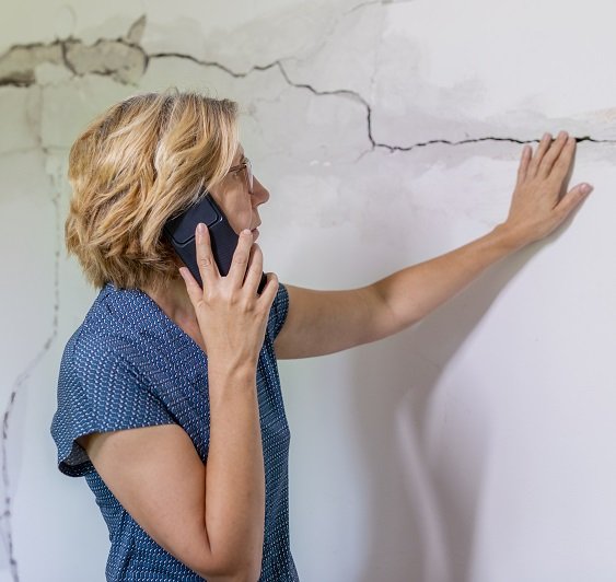 Woman looking at a wall damaged after the earthquake. She using smart phone for communication and for photography. Damage assessment and consultation